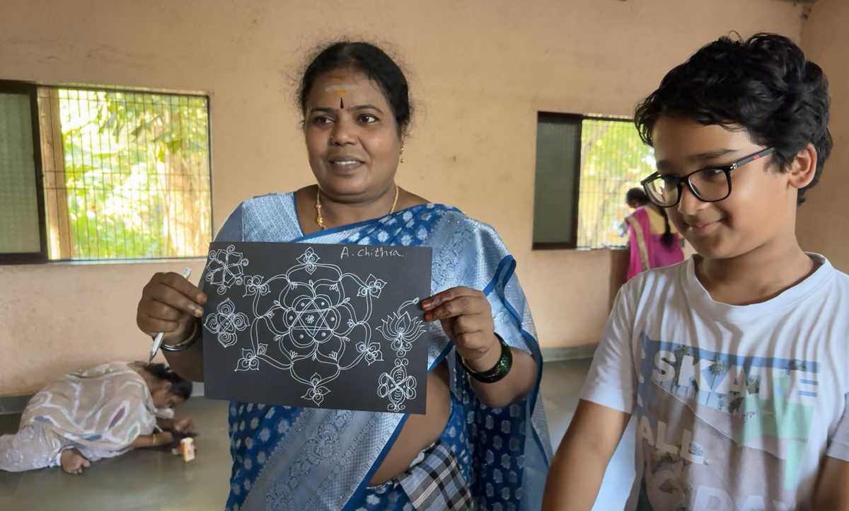 Two people holding up a completed white-on-black kolam design.